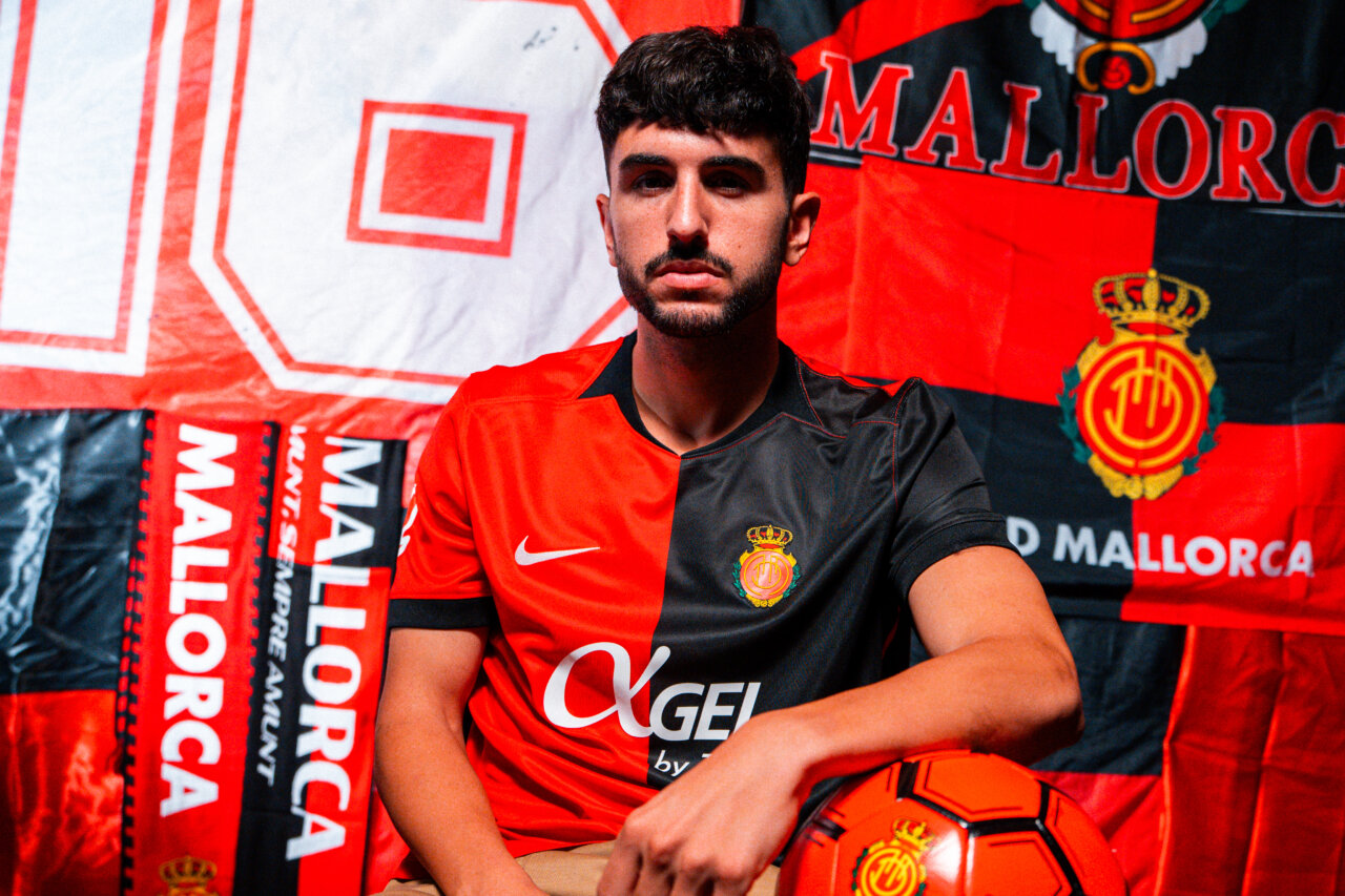 Jugador del Mallorca con nueva camiseta roja y negra en fondo de banderas