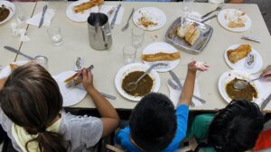 Ni&ntilde;os comiendo en un comedor escolar con platos vac&iacute;os y utensilios.