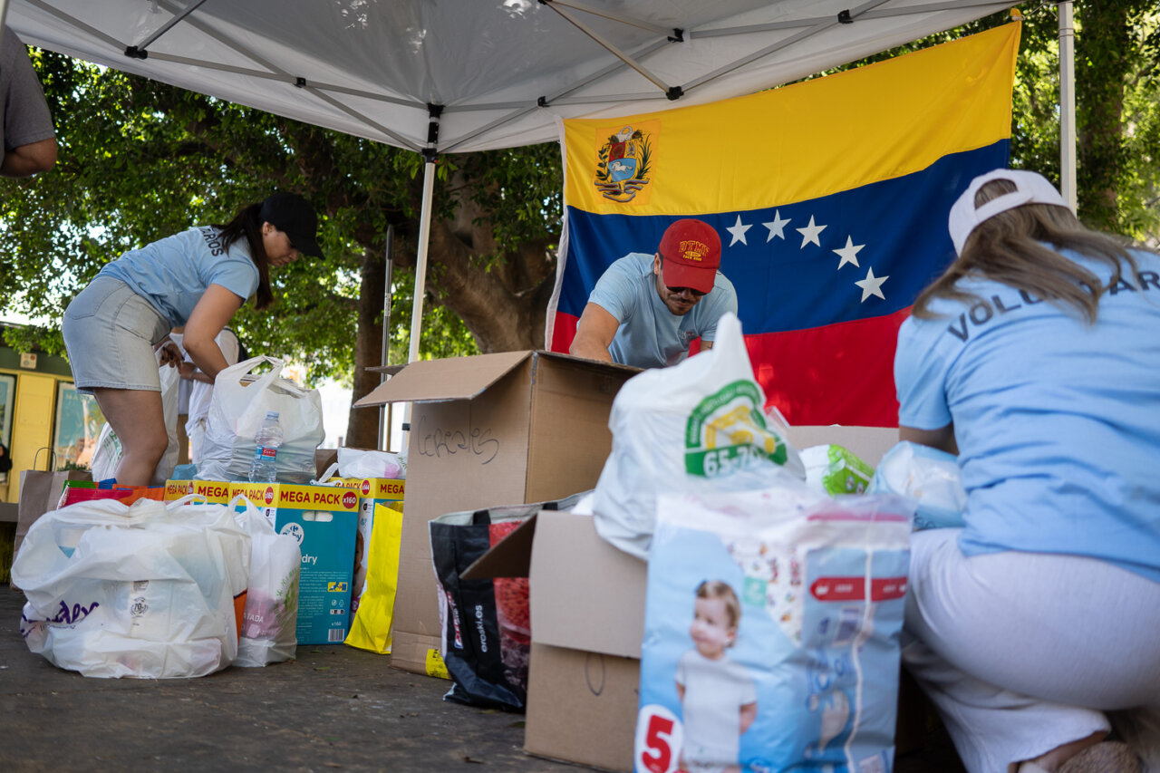 Voluntarios organizando donaciones bajo una carpa con la bandera de Venezuela.