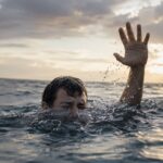 Hombre en el agua levantando la mano en se&ntilde;al de auxilio