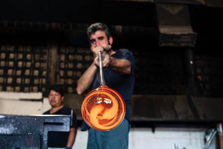 Artesano soplando vidrio caliente en un taller de vidrio.