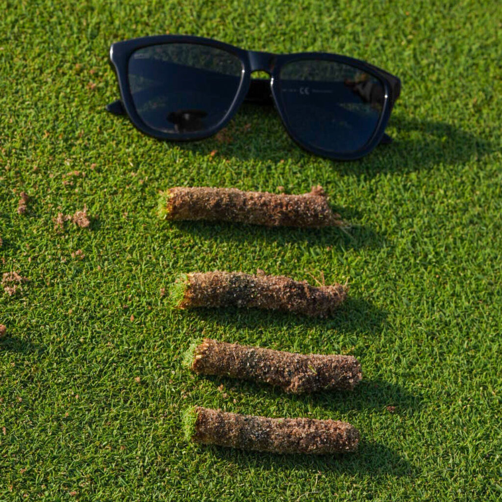 Proceso de pinchado en un green de golf con césped y herramientas