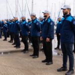Grupo de agentes de Frontex alineados en un puerto con barcos al fondo