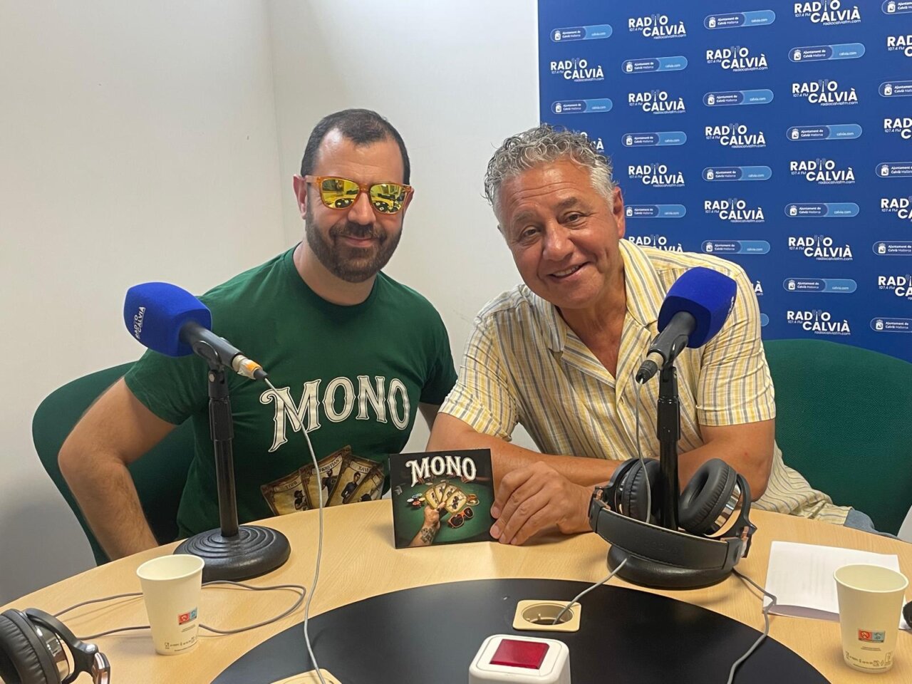 Dos hombres sonrientes en una entrevista de radio con micrófonos y un álbum