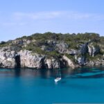 Vista de una isla balear con agua turquesa y un barco