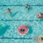 Personas disfrutando en una piscina con flotadores de frutas
