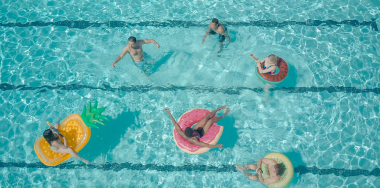 Personas disfrutando en una piscina con flotadores de frutas