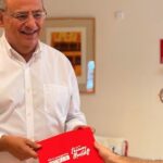 Alfonso Rodríguez sonríe mientras sostiene un documento rojo en una reunión.