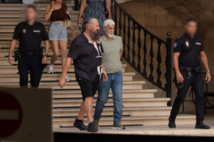 Dos hombres caminando por escaleras con policías en el fondo