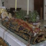 Escultura de la Virgen Mar&iacute;a muerta en un altar con velas y decoraciones