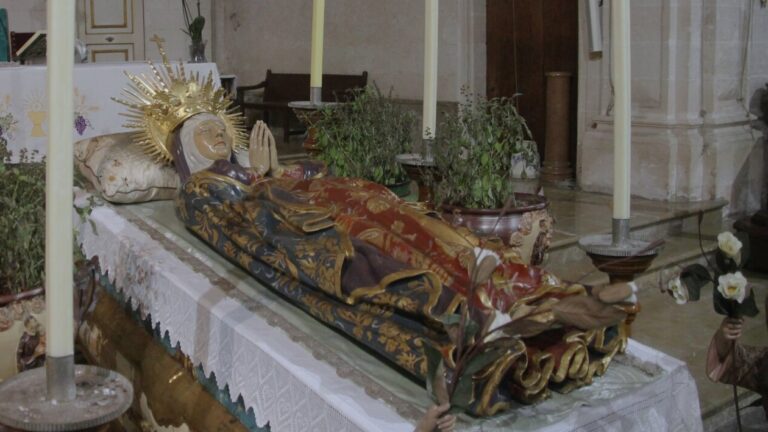 Escultura de la Virgen María muerta en un altar con velas y decoraciones