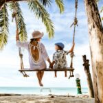 Mujer y niño en un columpio en la playa bajo palmeras