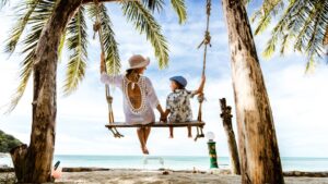 Mujer y niño en un columpio en la playa bajo palmeras
