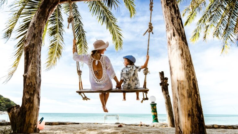 Mujer y niño en un columpio en la playa bajo palmeras